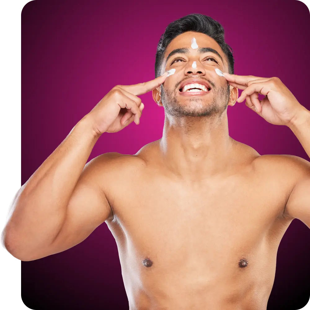 A shirtless man smiling and applying sunscreen